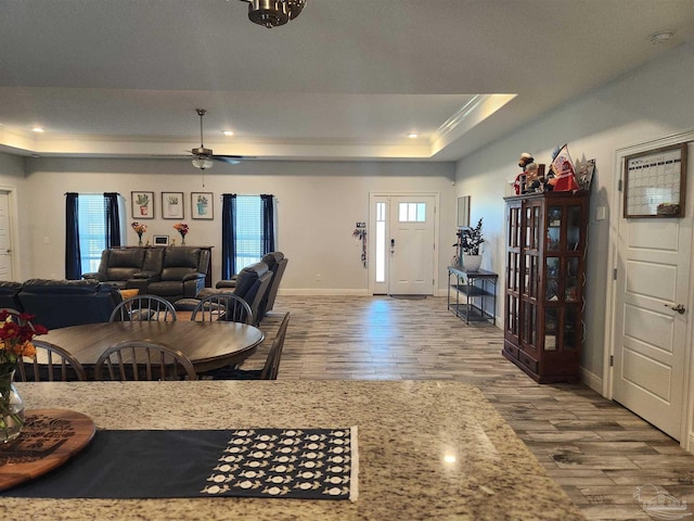 dining room featuring ceiling fan, light hardwood / wood-style floors, a raised ceiling, and a healthy amount of sunlight