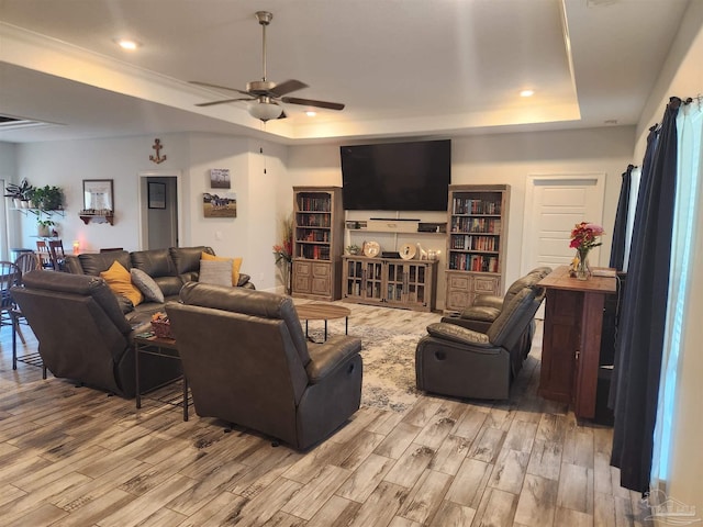 living room with ceiling fan, ornamental molding, light hardwood / wood-style flooring, and a tray ceiling