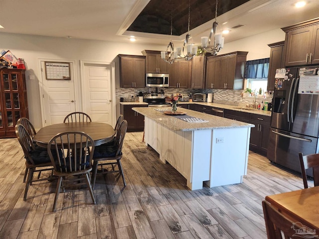 kitchen featuring light stone countertops, decorative light fixtures, a kitchen island, stainless steel appliances, and a chandelier