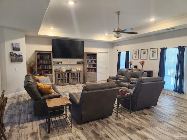 living room with hardwood / wood-style floors, a raised ceiling, ceiling fan, and ornamental molding