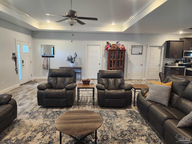 living room with a tray ceiling, ceiling fan, light hardwood / wood-style flooring, and ornamental molding