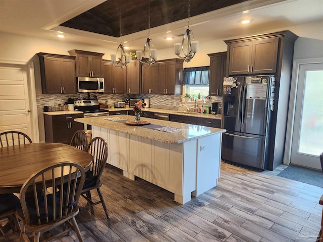 kitchen featuring a tray ceiling, decorative light fixtures, a kitchen island, dark brown cabinets, and stainless steel appliances