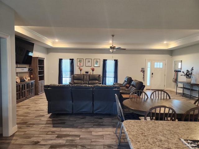 living room with a raised ceiling, ceiling fan, crown molding, and dark wood-type flooring