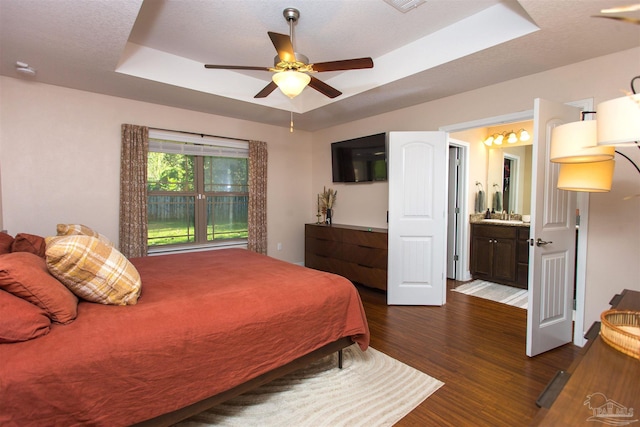 bedroom featuring a raised ceiling, ceiling fan, dark hardwood / wood-style floors, a textured ceiling, and connected bathroom