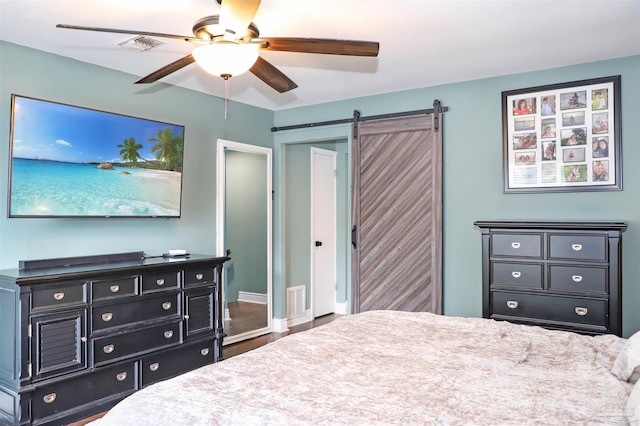 bedroom with a barn door, wood-type flooring, and ceiling fan