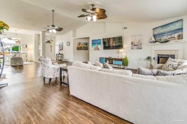 living room featuring a tiled fireplace, lofted ceiling, dark hardwood / wood-style floors, and ceiling fan with notable chandelier