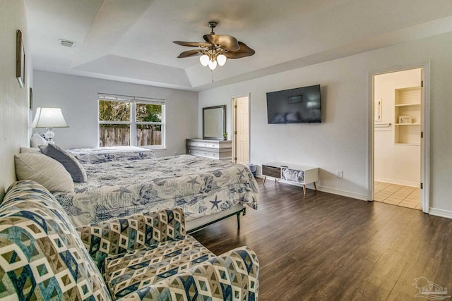 bedroom with dark hardwood / wood-style floors, ceiling fan, and a tray ceiling