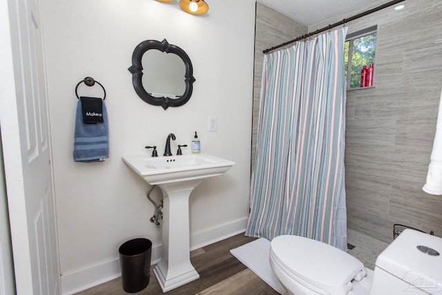 bathroom featuring toilet, a sink, wood finished floors, tiled shower, and baseboards