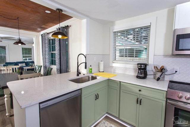 kitchen with a sink, tasteful backsplash, stainless steel appliances, a peninsula, and green cabinetry