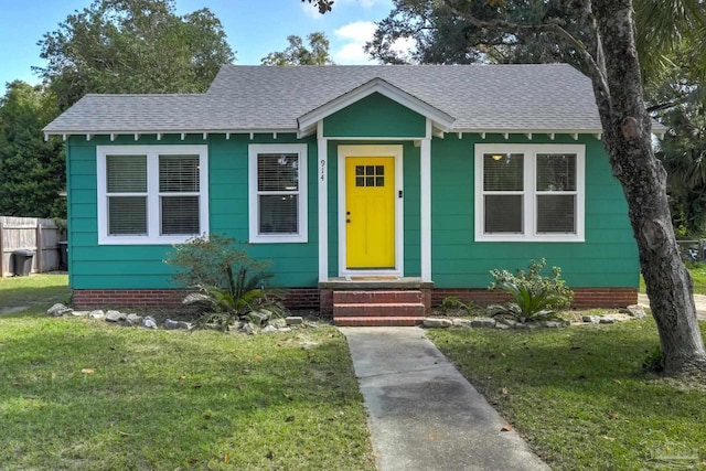 bungalow-style house featuring entry steps, fence, a front lawn, and roof with shingles