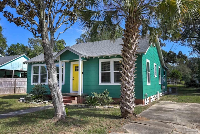 bungalow-style house with central AC unit, fence, a front yard, and a shingled roof