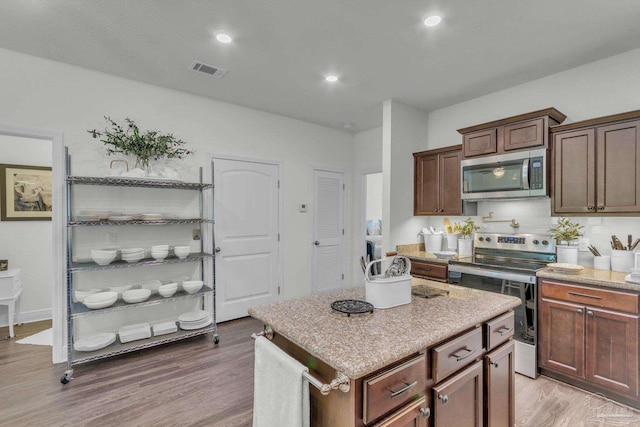 kitchen with visible vents, a center island, appliances with stainless steel finishes, light stone counters, and light wood finished floors