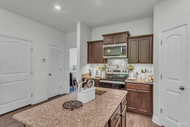 kitchen featuring light stone countertops, light wood-type flooring, a kitchen island, stainless steel appliances, and backsplash