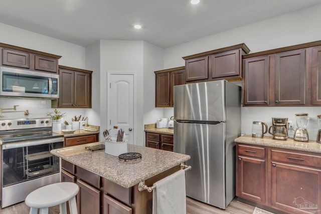 kitchen featuring stainless steel appliances, tasteful backsplash, light stone countertops, and light wood-style floors