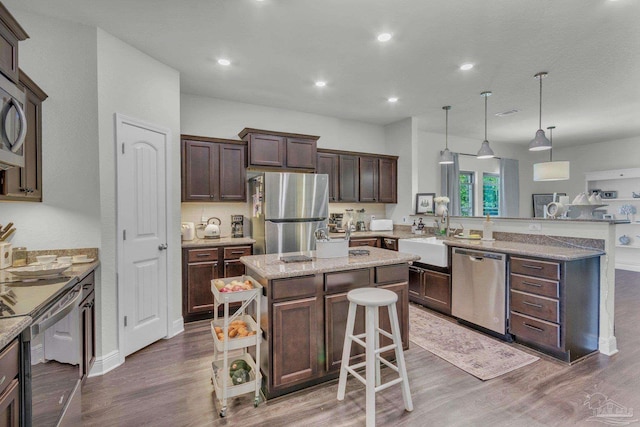 kitchen featuring a peninsula, dark wood-style floors, dark brown cabinets, stainless steel appliances, and a sink