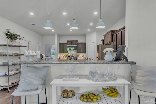 kitchen with a kitchen breakfast bar, dark brown cabinets, wood finished floors, hanging light fixtures, and stainless steel appliances