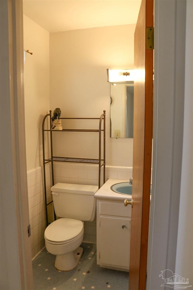 bathroom with tile walls, tile patterned floors, toilet, and vanity