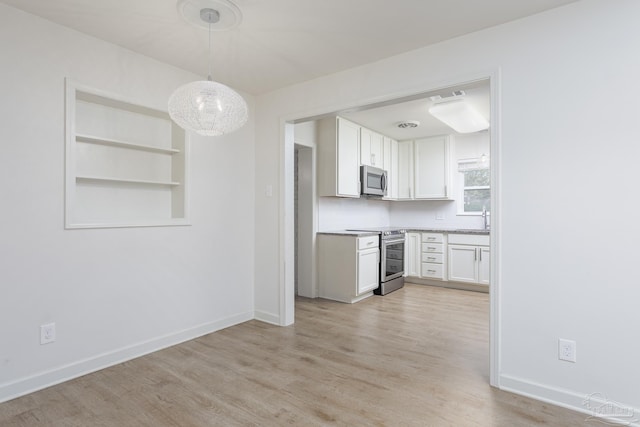 kitchen featuring stainless steel appliances, pendant lighting, sink, white cabinetry, and light wood-type flooring