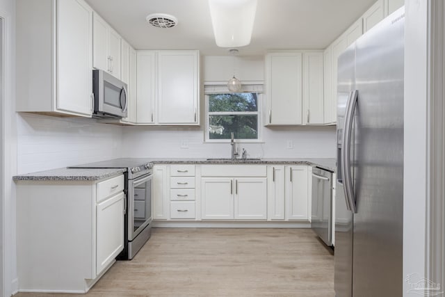 kitchen with white cabinets, light hardwood / wood-style floors, appliances with stainless steel finishes, and stone counters