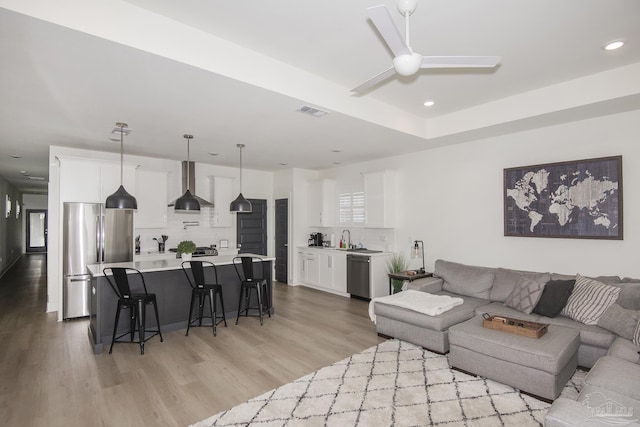 living room with light wood-type flooring, ceiling fan, and sink