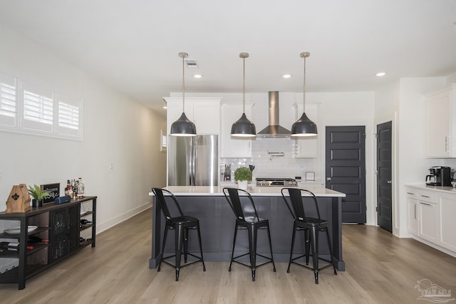 kitchen featuring white cabinetry, wall chimney exhaust hood, light hardwood / wood-style floors, decorative light fixtures, and appliances with stainless steel finishes