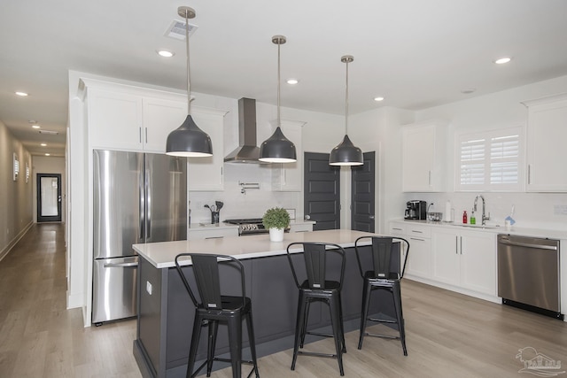 kitchen featuring appliances with stainless steel finishes, wall chimney range hood, light hardwood / wood-style flooring, a center island, and white cabinetry