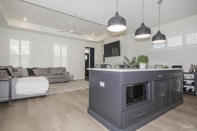 kitchen featuring ceiling fan, an island with sink, decorative light fixtures, and light hardwood / wood-style flooring