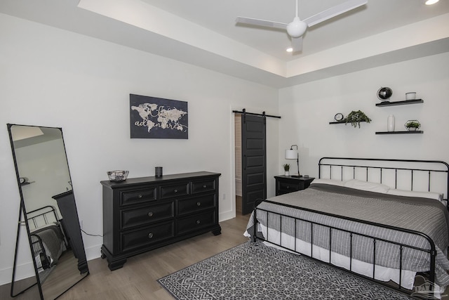 bedroom featuring ceiling fan, a barn door, and wood-type flooring