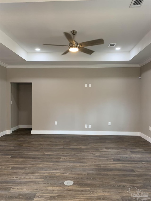 spare room with dark wood-style floors, a tray ceiling, visible vents, and baseboards