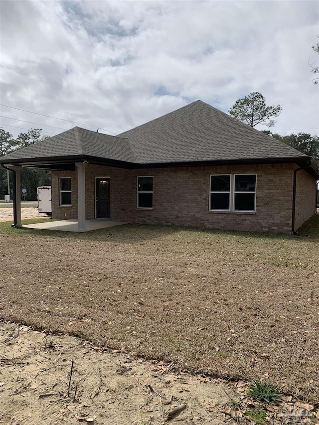 back of property featuring a patio area, a shingled roof, a yard, and brick siding