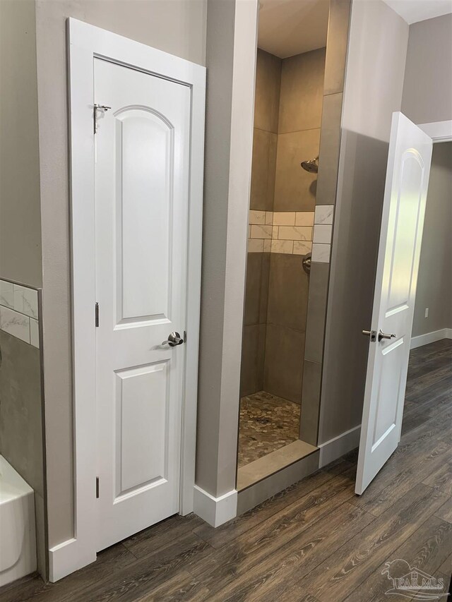 bathroom with a tile shower, wood finished floors, and baseboards