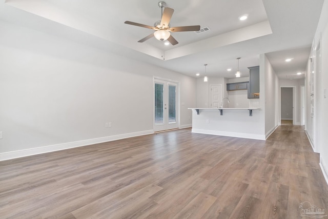 unfurnished living room with ceiling fan, hardwood / wood-style flooring, a tray ceiling, sink, and french doors