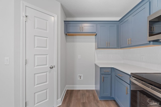 kitchen with decorative backsplash, stainless steel appliances, hardwood / wood-style floors, and blue cabinetry