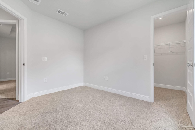 unfurnished bedroom with light colored carpet, a closet, and a spacious closet