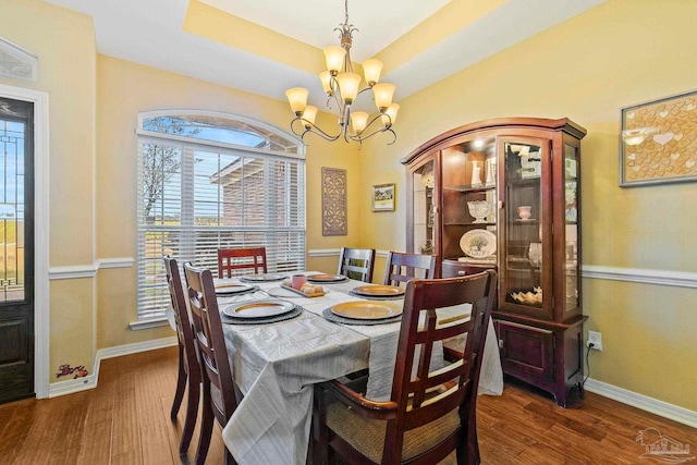 dining area featuring a raised ceiling, dark wood-type flooring, and a notable chandelier