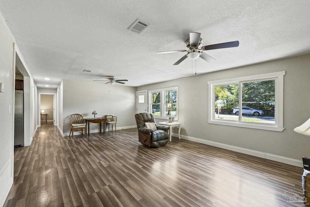 living area featuring visible vents, ceiling fan, a textured ceiling, wood finished floors, and baseboards