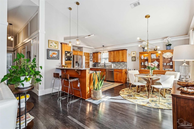 kitchen with kitchen peninsula, appliances with stainless steel finishes, decorative backsplash, vaulted ceiling, and a breakfast bar