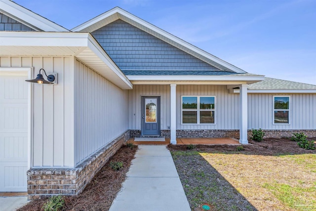 view of exterior entry featuring board and batten siding, a shingled roof, and covered porch
