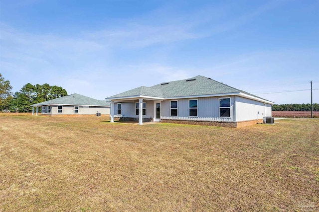 rear view of property with cooling unit, a lawn, and roof with shingles