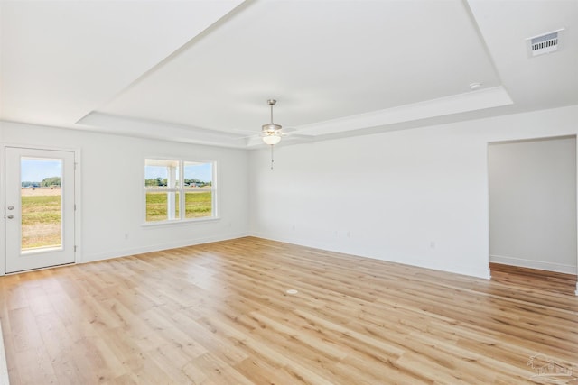 empty room with a raised ceiling, light wood-style flooring, and visible vents