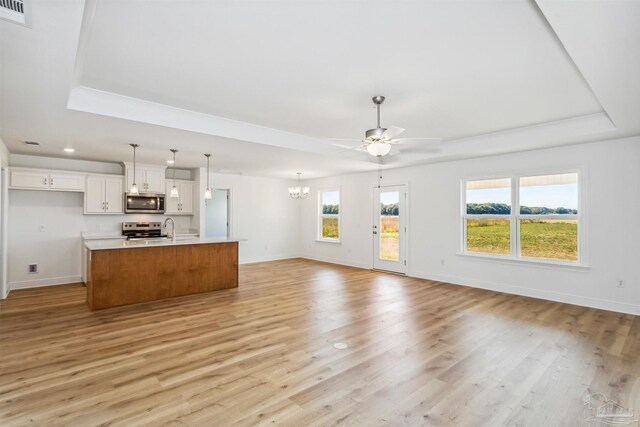 unfurnished living room with a tray ceiling, baseboards, visible vents, light wood-style floors, and ceiling fan with notable chandelier