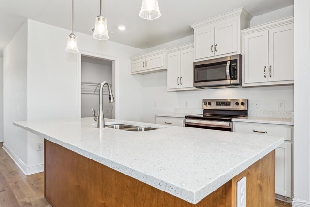 kitchen with a sink, light wood-type flooring, white cabinetry, an island with sink, and appliances with stainless steel finishes