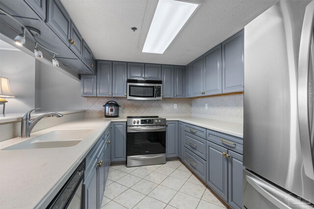 kitchen with light tile patterned flooring, appliances with stainless steel finishes, sink, backsplash, and a textured ceiling