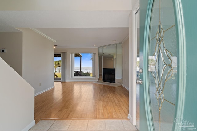 entryway with light wood-style floors, a fireplace, baseboards, and crown molding