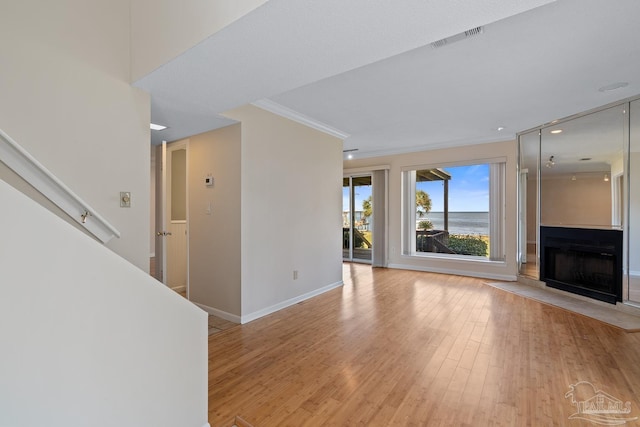 unfurnished living room with ornamental molding, a large fireplace, visible vents, and light wood-style flooring