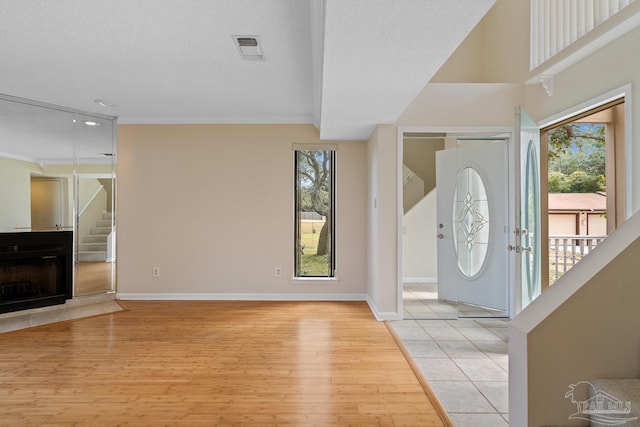 entryway with visible vents, light wood-style flooring, a fireplace with flush hearth, stairs, and crown molding