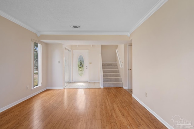 foyer with ornamental molding, visible vents, light wood-style flooring, and stairs