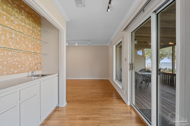 corridor featuring visible vents, light wood-style flooring, rail lighting, crown molding, and a sink