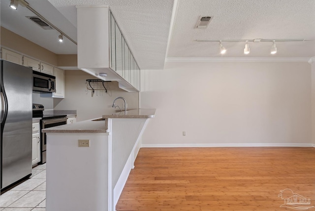 kitchen with a textured ceiling, light wood-style flooring, a peninsula, a sink, and appliances with stainless steel finishes