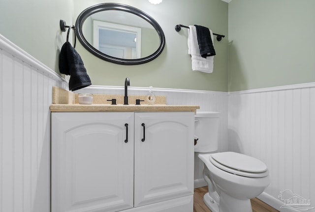 half bath featuring a wainscoted wall, wood finished floors, a sink, and toilet